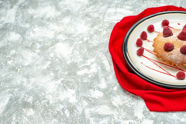 Bottom half view berry cake on white oval plate red shawl on grey surface fre space