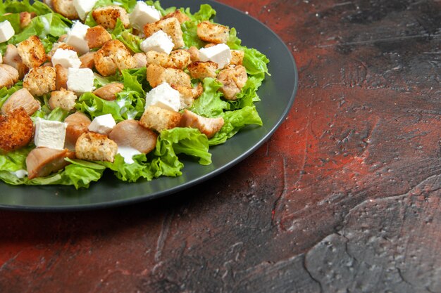 Bottom half view caesar salad on oval plate on dark red table