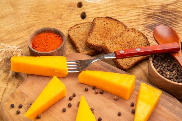 Bottom half view cheese on fork slices of cheese on cutting board red pepper slices of bread black pper in bowl on wooden table