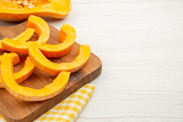 Bottom half view chopped butternut squash on chopping board on yellow white checkered kitchen towel on grey table free space