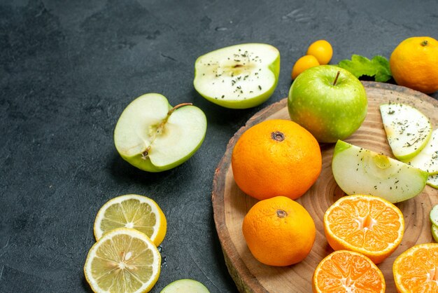 Нижняя половина вида нарезанных яблок и мандаринов на деревенской сервировочной доске, нарезанных ломтиками лимона на темном столе