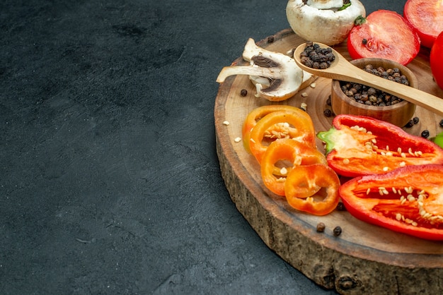 Нижняя половина вида свежие овощи грибы черный перец в миске деревянной ложкой красные помидоры болгарский перец на деревянной доске на темном столе со свободным пространством