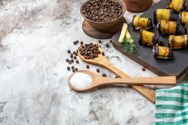 Bottom half view grilled eggplant rolls on wood chopping board spices in wooden spoons on nude background free space