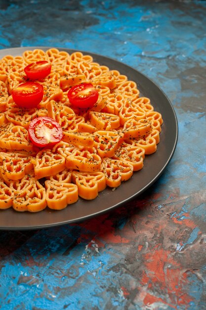 Bottom half view italian pasta hearts cut cherry tomatoes on black oval plate on blue surface