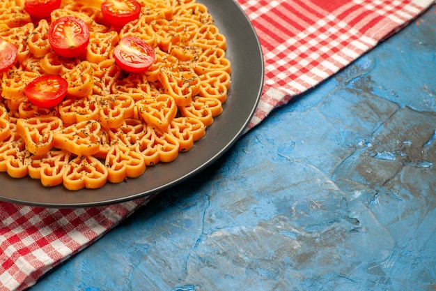 Mezza vista inferiore cuori di pasta italiana tagliati pomodorini su piatto ovale su tavolo a scacchi bianco rosso
