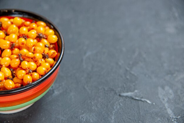 Bottom half view sea buckthorn in bowl on dark red surface copy place