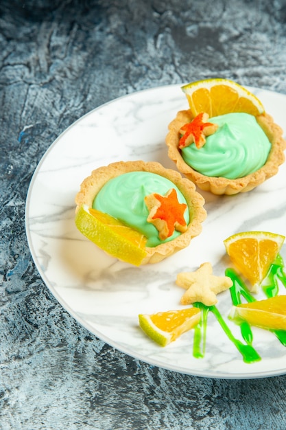 Bottom half view small tarts with green pastry cream and lemon slice on plate on dark surface