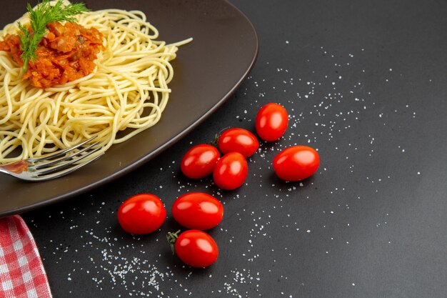 下半分のビュースパゲッティ、プレートにソース、黒いテーブルにチェリートマト