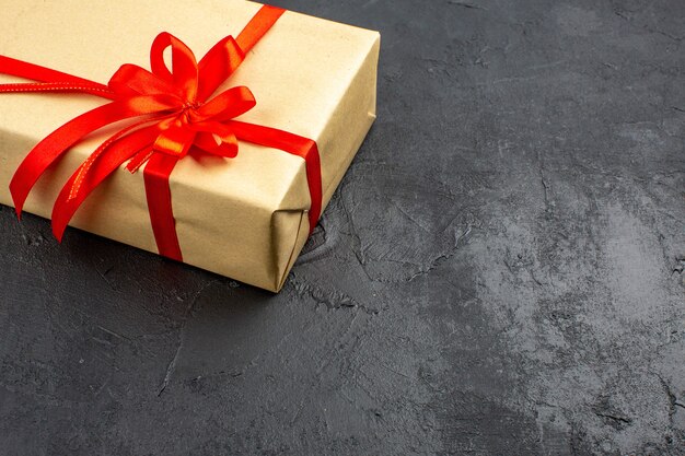 Bottom half view xmas gift in brown paper tied with red ribbon on dark background