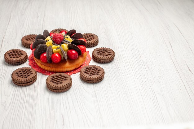 Bottom left side view berry cake on the red oval lace doily rounded with cookies on the white wooden table with free space