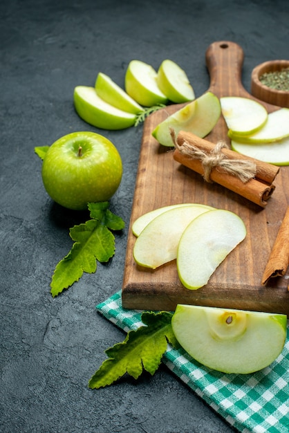 Вид снизу ломтики яблока и корица на разделочной доске сухой порошок мяты в миске скатерть зеленого яблока на темном столе