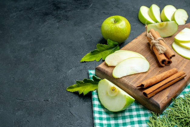 Bottom view apple slices and cinnamon on cutting board dried mint powder in small bowl apple pine tree branches on dark table free space