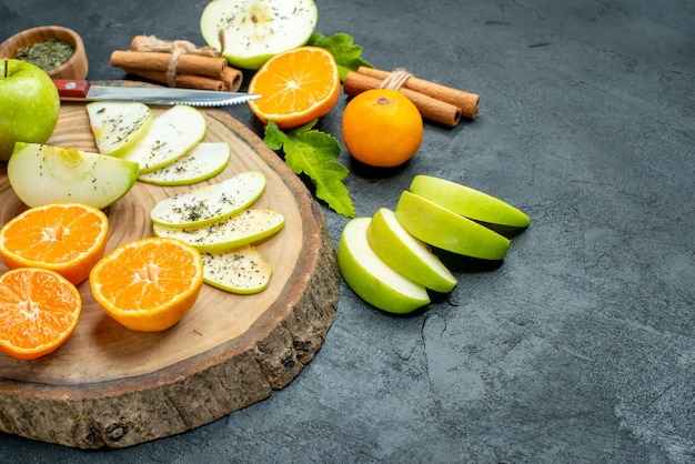 Bottom view apple and tangerines slices knife on wood board cinnamon sticks tied with rope dried mint powder in bowl on black table