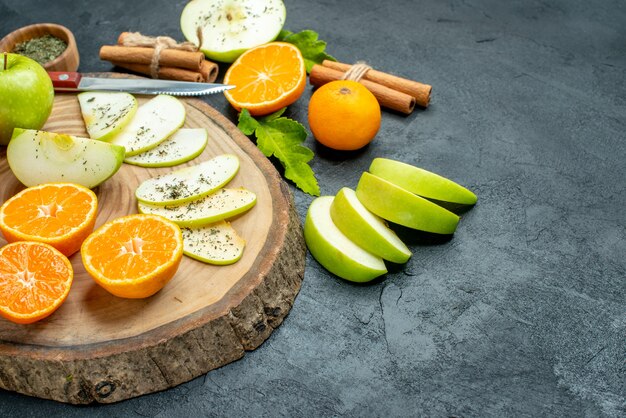 Bottom view apple and tangerines slices knife on wood board cinnamon sticks tied with rope dried mint powder in bowl on black table