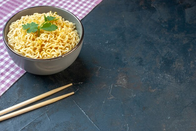 Bottom view asian ramen noodles with coriander in bowl on pink white checkered tablecloth chopsticks on dark table with free space