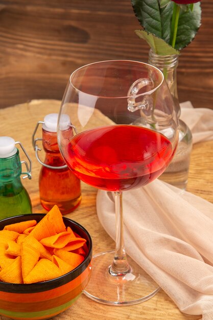 Bottom view balloon wine glass chips in bowl red and green bottles on brown surface