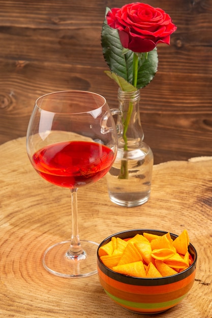 Free photo bottom view balloon wine glass chips in bowl red rose on brown surface