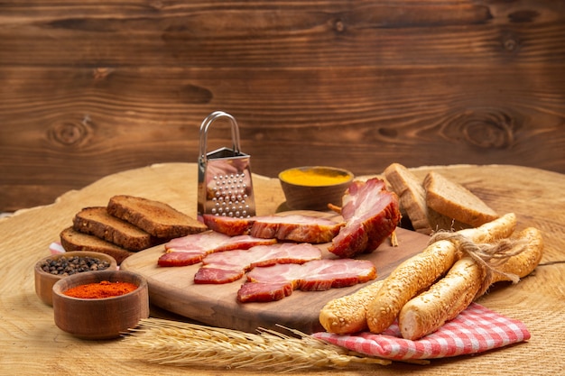 Bottom view becon slices on wood board white and brown bread box grater spices on wooden table