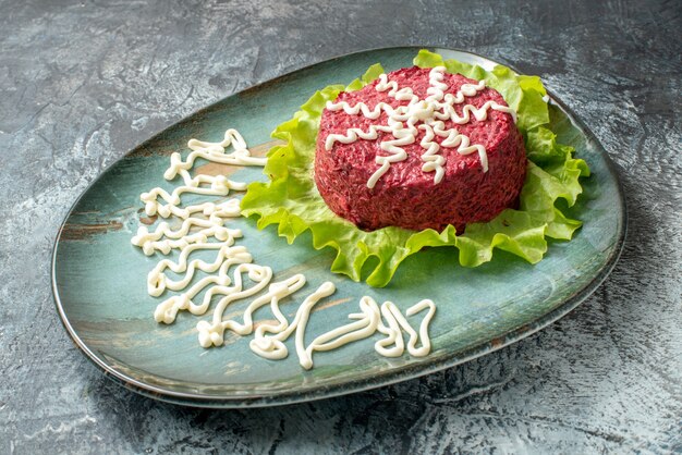 Bottom view beet salad decorated with mayonnasie and lettuce on plate on grey table