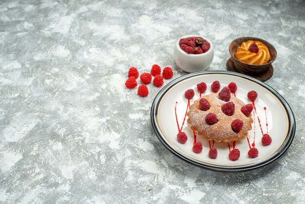 Bottom view berry cake on white oval plate biscuit in wooden bowl raspberries in bowl on grey surface free space