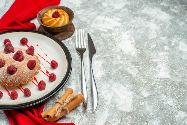 Bottom view berry cake on white oval plate red shawl biscuit fork and dinner knife cinnamon sticks on grey surface with copy space