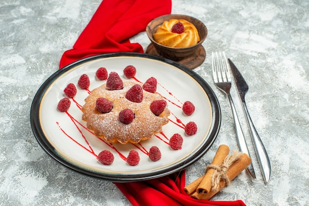 회색 표면에 흰색 타원형 접시 빨간 목도리 비스킷 포크와 저녁 식사 칼 계피 스틱에 하단보기 베리 케이크