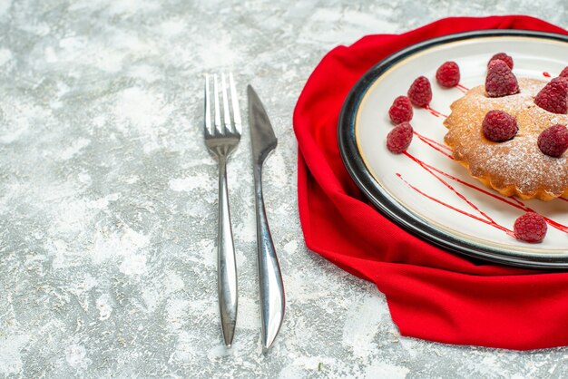 Bottom view berry cake on white oval plate red shawl fork and dinner knife on grey surface free space