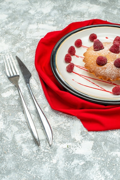 Bottom view berry cake on white oval plate red shawl fork dinner knife on grey surface