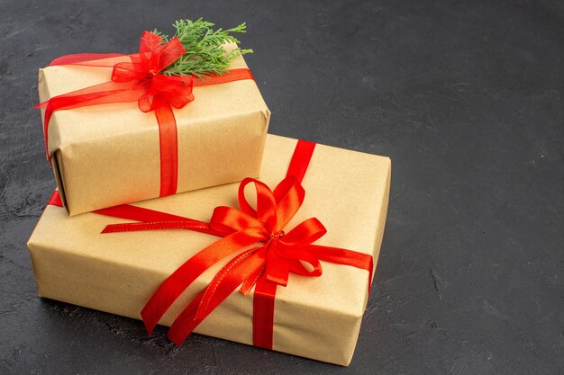 Bottom view big and small xmas gifts in brown paper tied with red ribbon on dark background free space