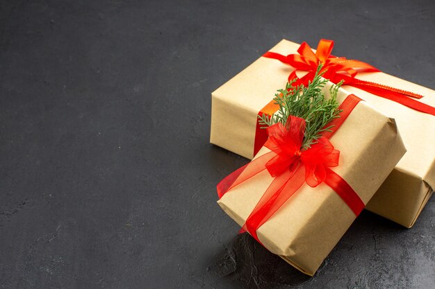 Bottom view big and small xmas gifts in brown paper tied with red ribbon on dark free space