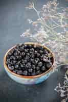 Free photo bottom view black currant in bowl dried flowers on isolated surface