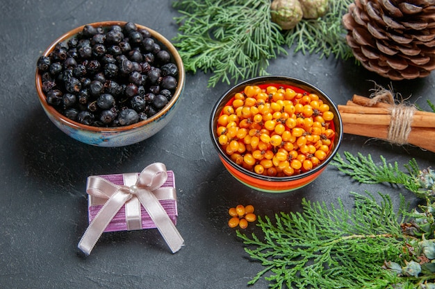 Bottom view black currant sea buckthorn in bowls pine branch cinnamon sticks on dark surface