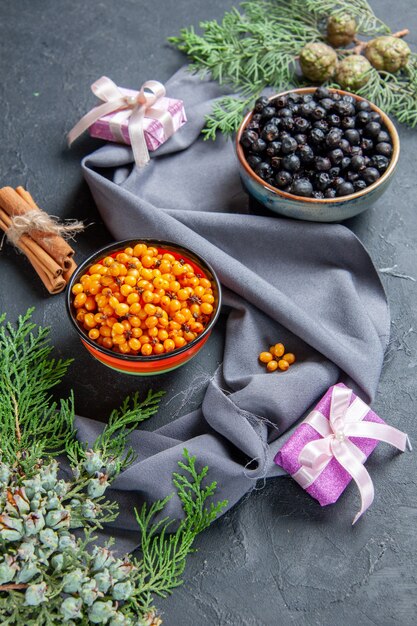 Bottom view black currant sea buckthorn in bowls pine branches purple shawl cinnamon on dark surface