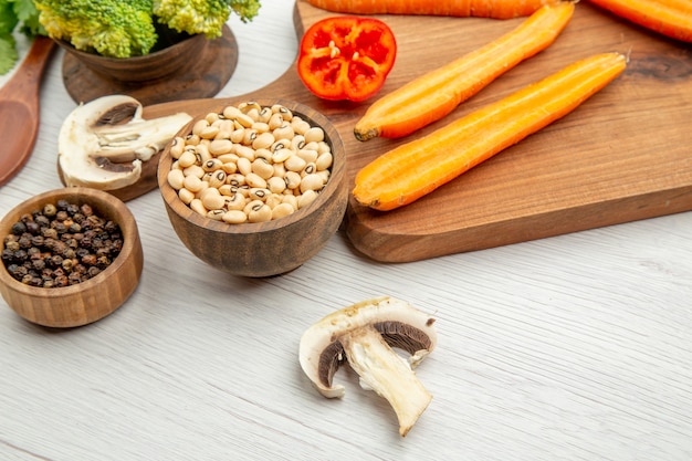 Bottom view black-eyed peas in wooden bowl mushrooms black pepper in bowls carrots on cutting board on table