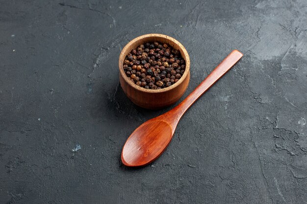 Bottom view black pepper bowl wooden spoon on dark surface copy place