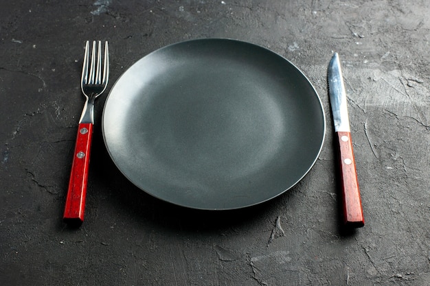 Вид снизу черная тарелка, вилка и нож на черной поверхности