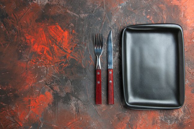 Bottom view black rectangular plate knife and fork on dark red table with copy space