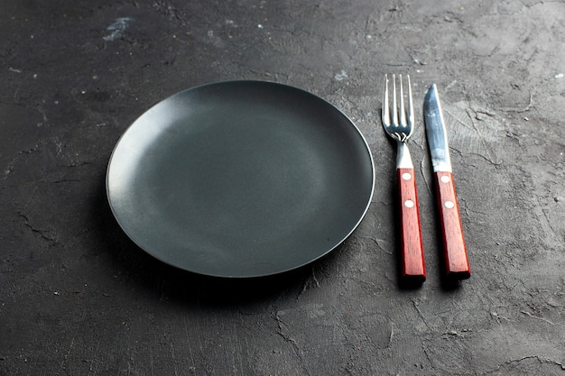 Вид снизу черное круглое блюдо вилкой и ножом на черной поверхности