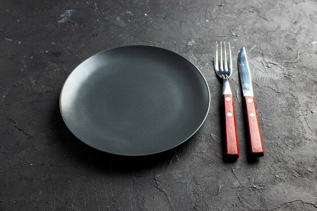 Вид снизу черное круглое блюдо вилкой и ножом на черной поверхности