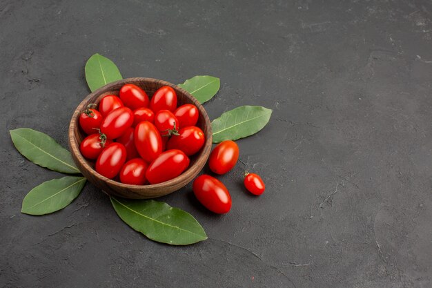 Bottom view a bowl of cherry tomatoes and bay leaves on the black table with copy space