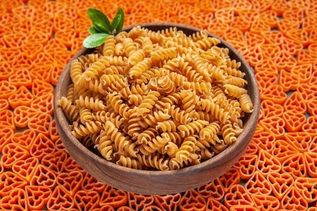 Bottom view a bowl of spirali pasta on heart shaped italian pasta on dark surface