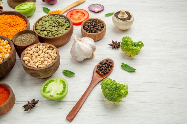 Bottom view bowls with beans seeds wooden spoons broccoli mushroom on grey table