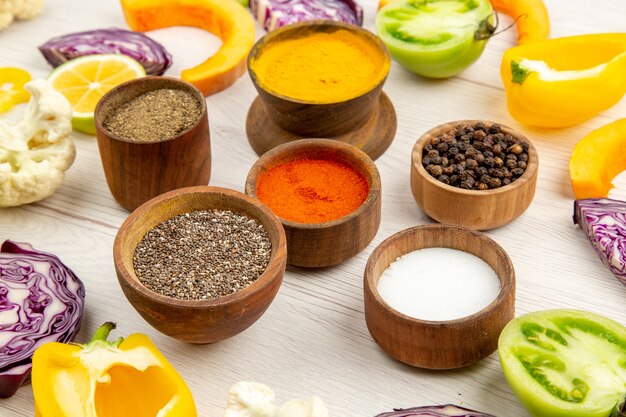 Bottom view bowls with spices cut bell pepper cauliflower cut pumpkin cut red cabbage cut green tomatoes on white table