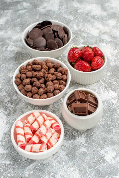 Bottom view bowls with white-red candies strawberries chocolates cereals and cacao on the grey-white background
