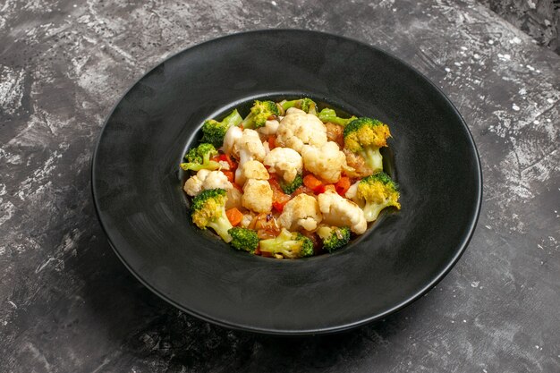 Bottom view broccoli and cauliflower salad on black oval plate on dark background