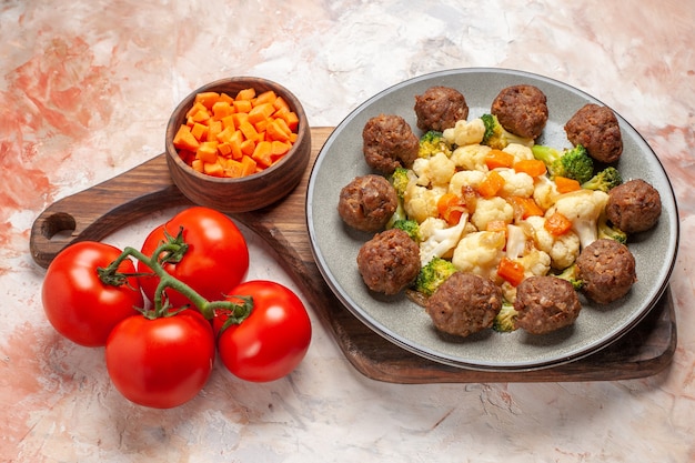 Bottom view broccoli and cauliflower salad and meatball on plate cutting carrot in bowl on cutting board tomatoes on nude background