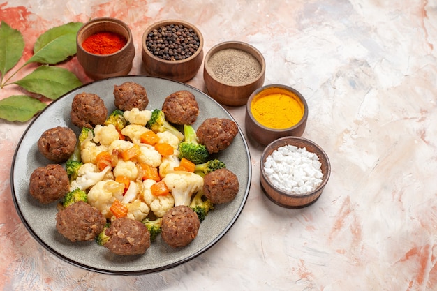 Free photo bottom view broccoli and cauliflower salad and meatball on plate different spices in small bowls on nude isolated background free place