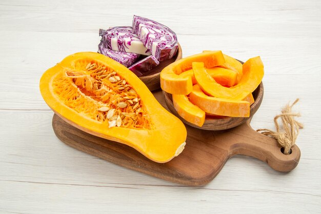 Bottom view butternut squash cut in half red cabbage and squash slices in bowls on cutting board on white table