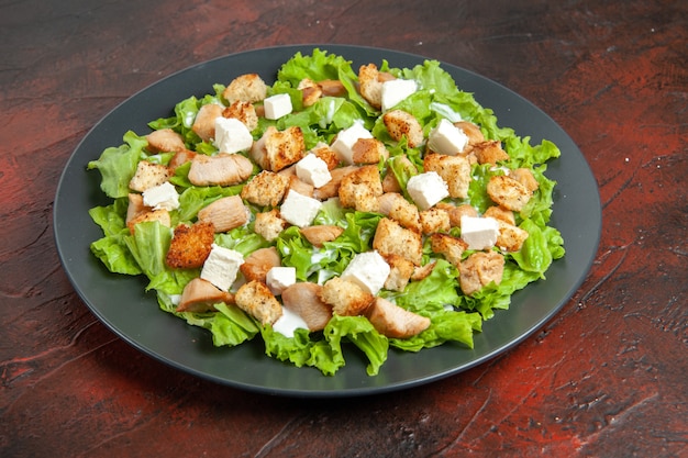 Bottom view caesar salad on oval plate on dark red table
