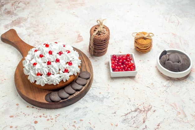 Bottom view cake with white pastry cream on cutting board bowl with berries and chocolate cookies tied with rope on light grey table